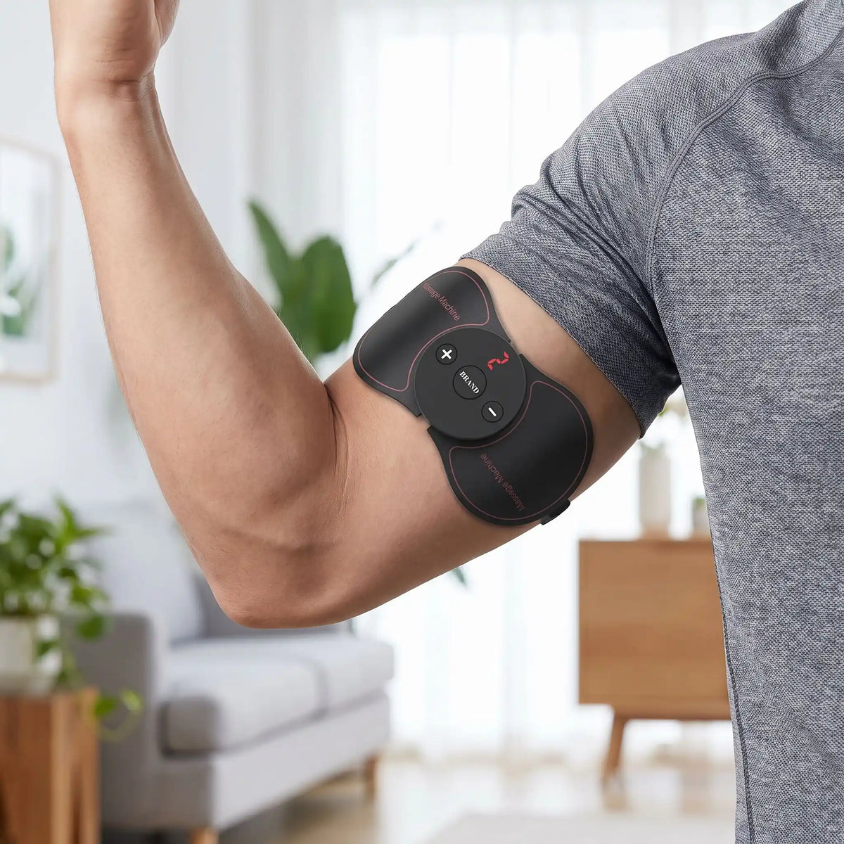 Un stimulateur musculaire EMS noir fixé sur le biceps contracté d'un homme portant un t-shirt gris