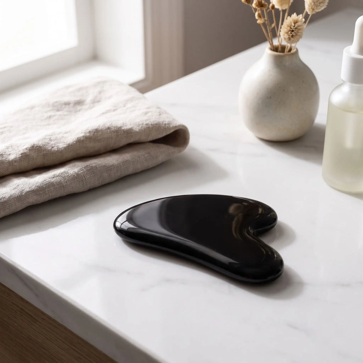 Gua sha en obsidienne noire en forme de cœur posé sur une table 