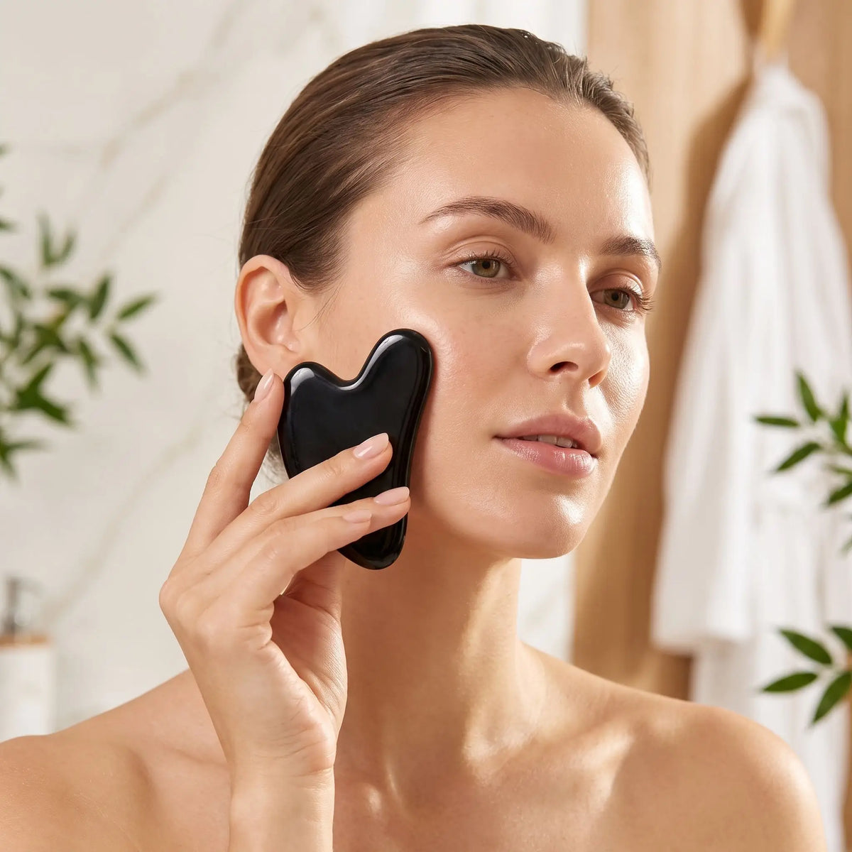 Femme utilisant un gua sha en obsidienne noire pour masser sa joue